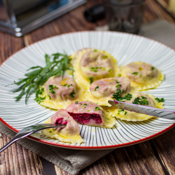 Beetroot and goats cheese ravioli pasta on a white striped plate with red rim. 