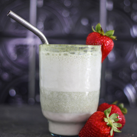 Layered strawberry matcha latte in a clear glass with a metal straw, topped with strawberry sliced