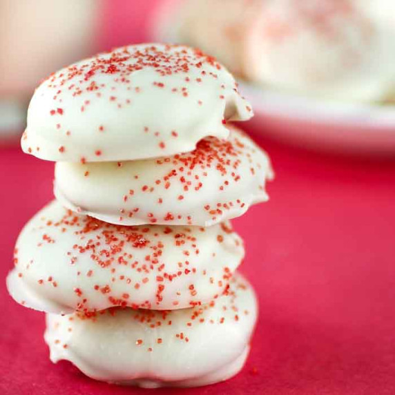 Side view of four Valentines day cookies stacked with a pink background.