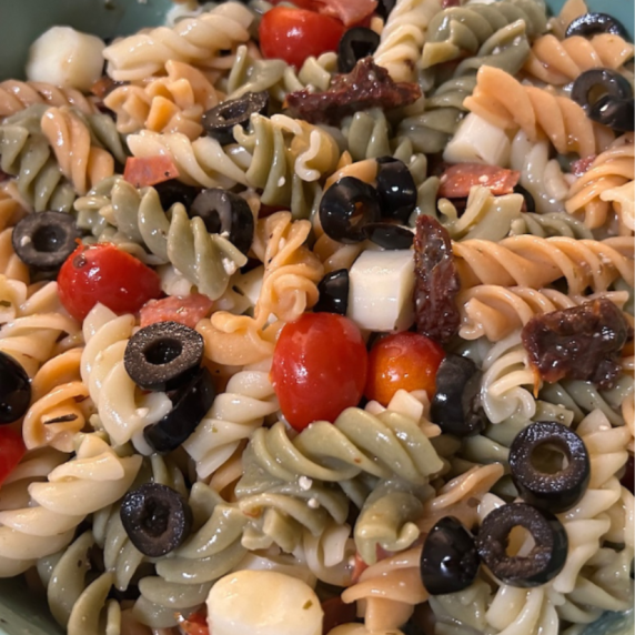 colorful pasta salad with rotini pasta, tomatoes, olives, cheese, sun-dried tomatoes, dressing
