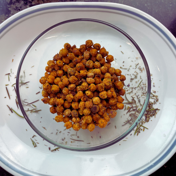 roasted chickpeas in a glass bowl with scattered herbs around it 