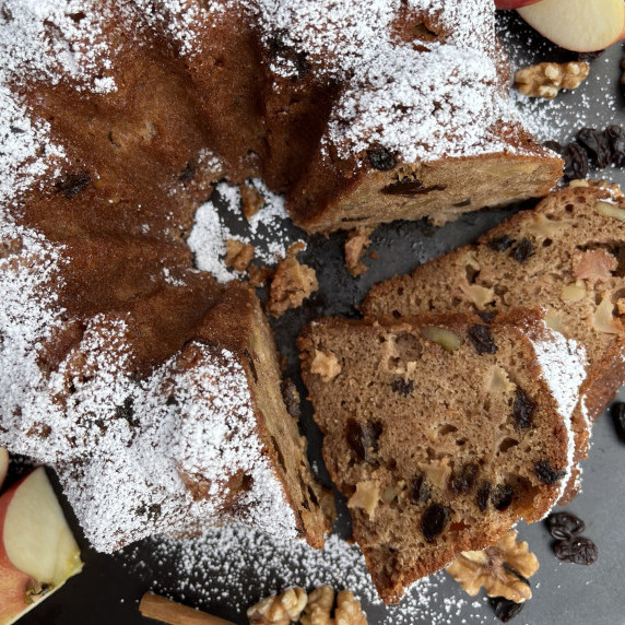 Apple Bundt cake sliced on a black board with walnut pieces, raisins and apple chunks.
