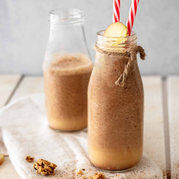 Two apple pie smoothies in milk jars with red and white straws and sliced apple.