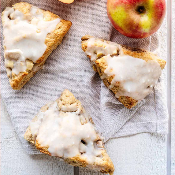 Overhead view of apple scones on a white wood table with a white napkin and apples.