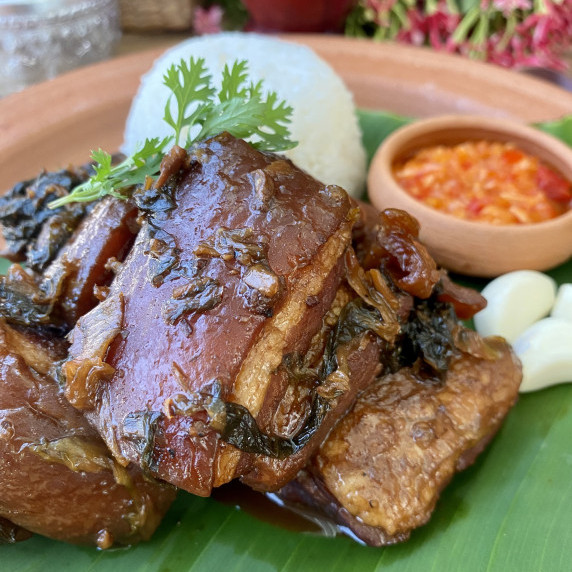 Braised pork belly with garlic and a red dipping sauce in the background.