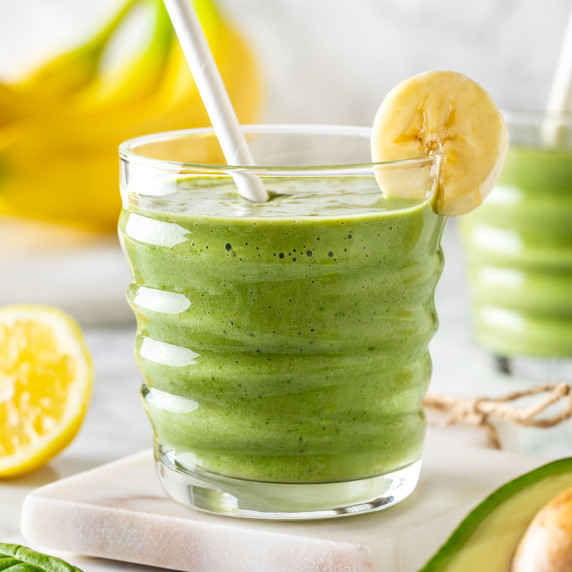 Glass with green avocado banana peanut butter smoothie decorated with a slice of banana