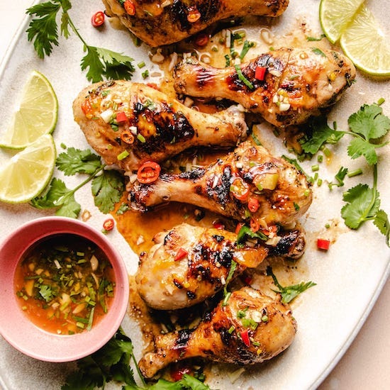 Grilled chicken drumsticks on a white plate with sweet chili BBQ sauce in a pink ramekin