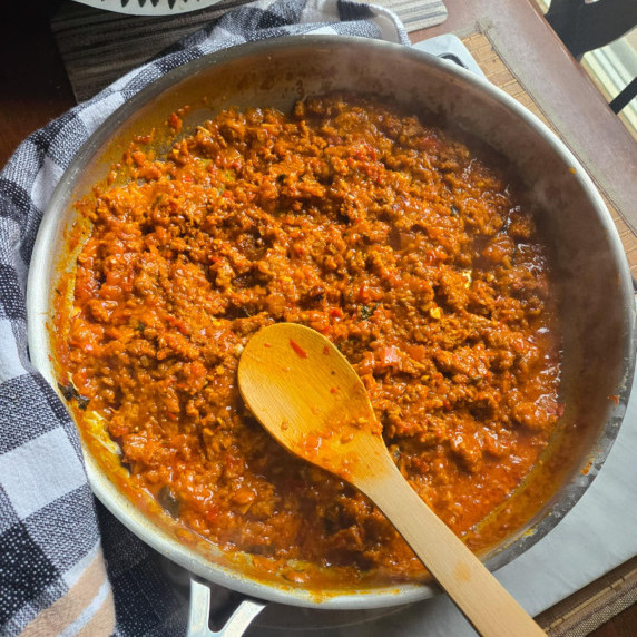 A skillet full of vibrant Bolognese sauce against a checkered towel.