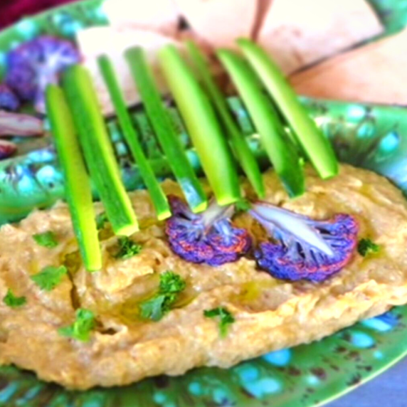 Baba Ganoush dip garnished with purple cauliflower and sliced cucumber on a green plate with pita
