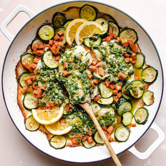 Baked cod sliced zucchini carrots lemons chives cilantro & parsley in white pot with wooden spoon
