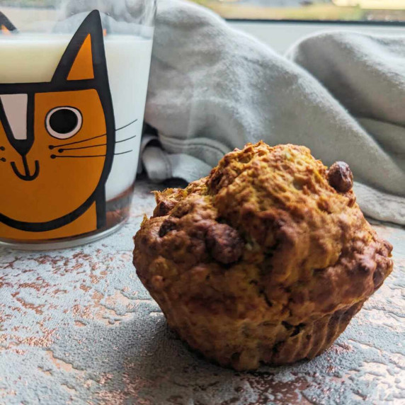 A banana and choc chip muffin alongside a glass of milk in a child's glass