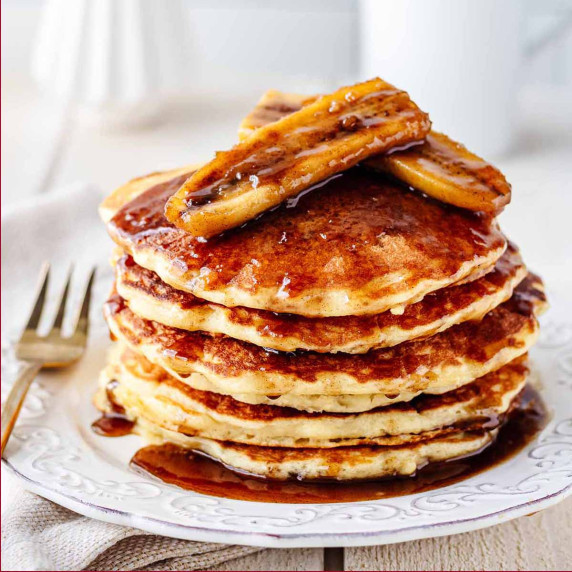 Stack of bananas Foster pancakes on a white plate with a gold fork.