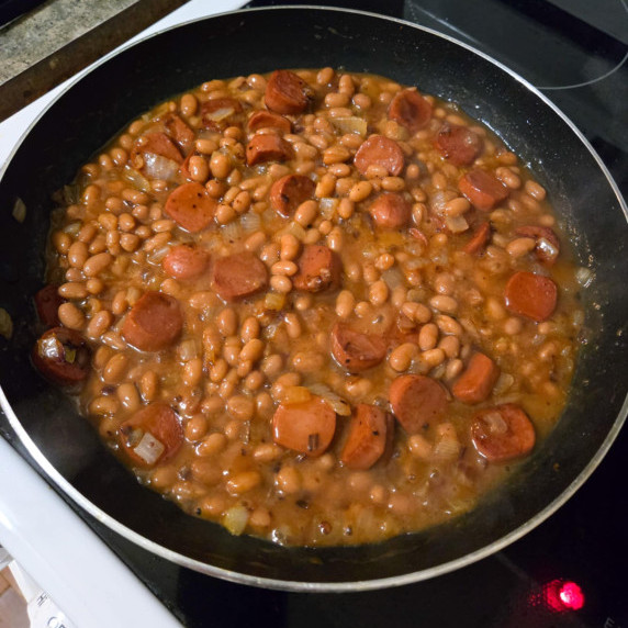 A skillet of saucy brown beans with hot dogs.