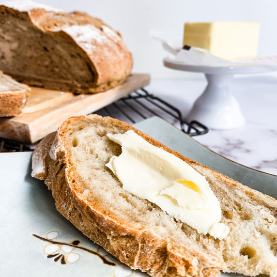 Slice of beer trub bread with butter in front of sliced loaf of bread and stick of butter on counter