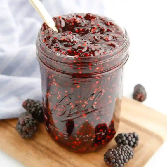 Blackberry jam from the side in a jar that is open with a spoon in the top.