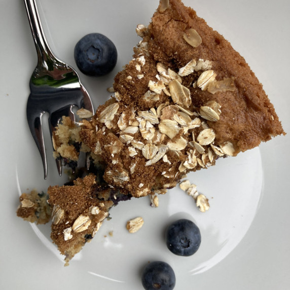Slice of blueberry coffee cake with fresh blueberries on a white plate.