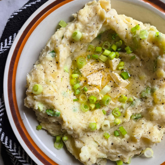 Creamy mashed potatoes with green onions & butter in a coloured, rimmed bowl