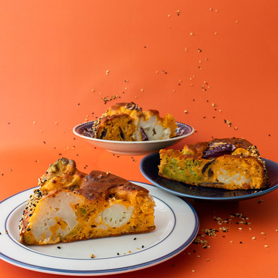 Three slices of cauliflower broccoli cake on a bright orange backdrop.