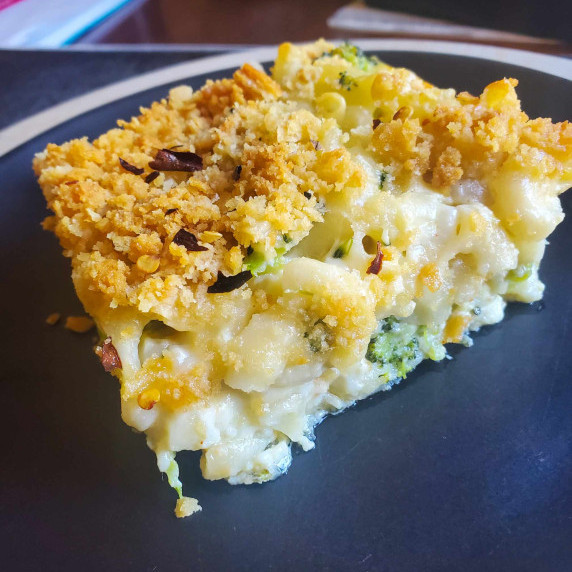 Creamy mac and cheese with a golden brown crust on a black plate.