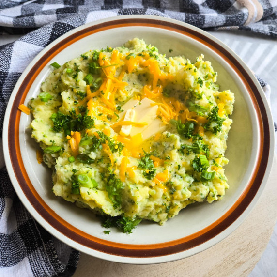A brown rimmed bowl filled with green mashed potatoes against a checkered towel.
