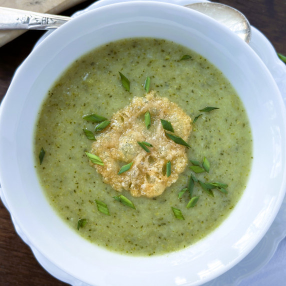 Broccoli leek soup garnished with a parmesan crisp and fresh chives in a white bowl.