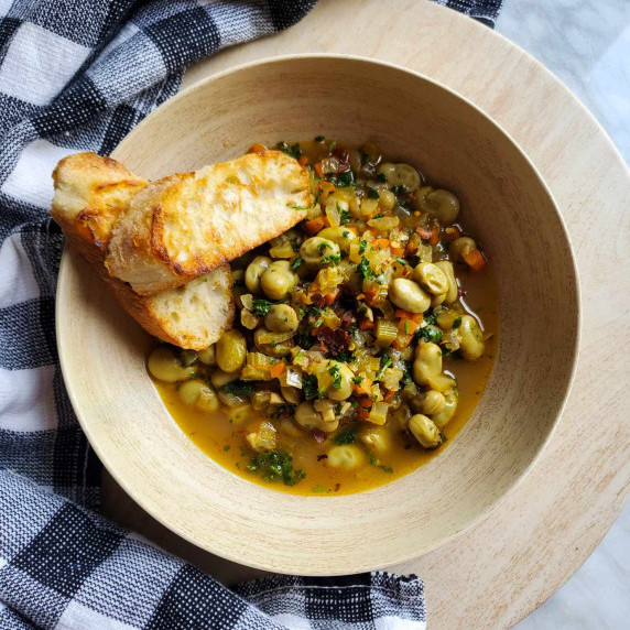 A wooden bowl filled with beans, golden grilled bread, and a black and white checkered towel.