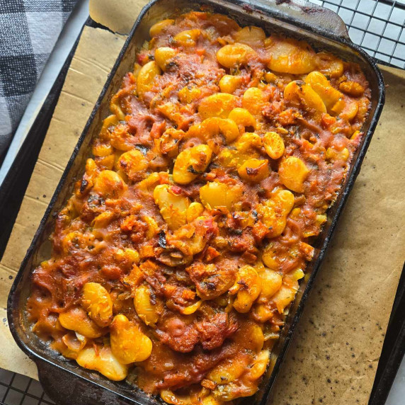 A baking dish full of golden butter beans on a brown parchment lined tray.