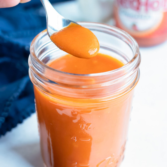 Buffalo Wing Sauce RECIPE stored in a Mason jar and with a spoon.