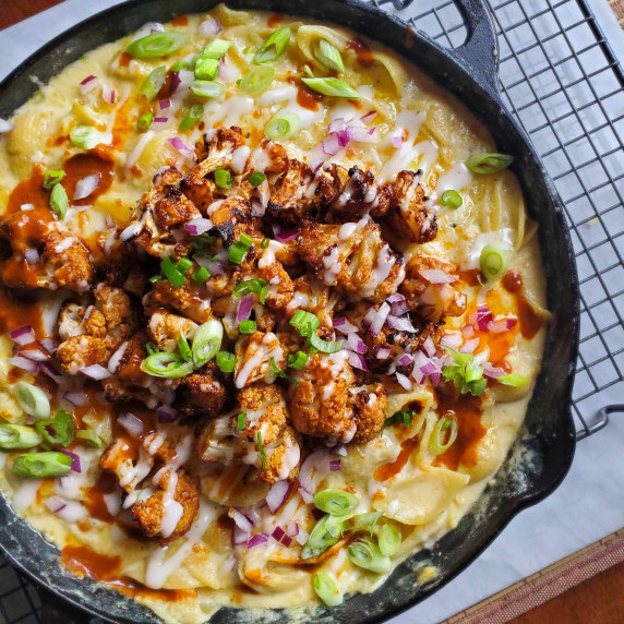 A skillet full of creamy shells and topped with deep red cauliflower and pops of colour from garnish