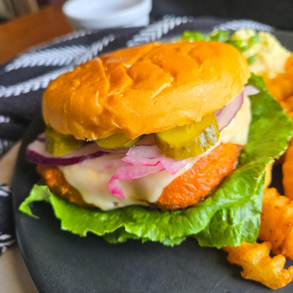 Buttery, golden brioche buns, green pickles, red onions, & crisp lettuce on a black plate