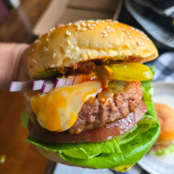A burger with melty cheese, bright veggies and sauces.