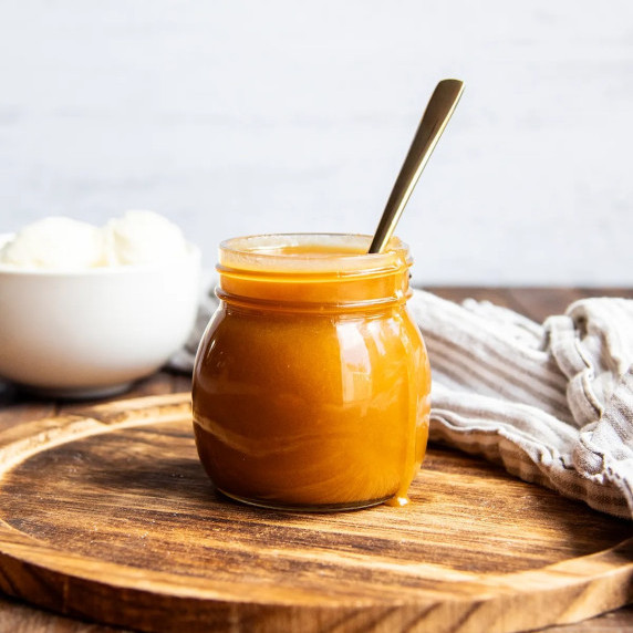 A photo of a glass container of butterscotch sauce with a spoon.