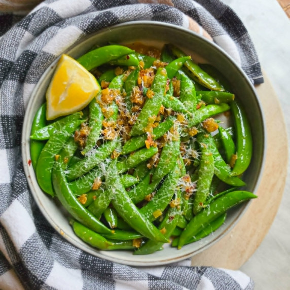 A bowl of bright green snap peas against a checkered towel.