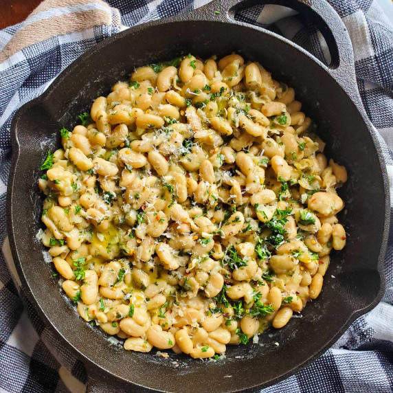 A black skillet full of creamy beans against a black and white cloth background.