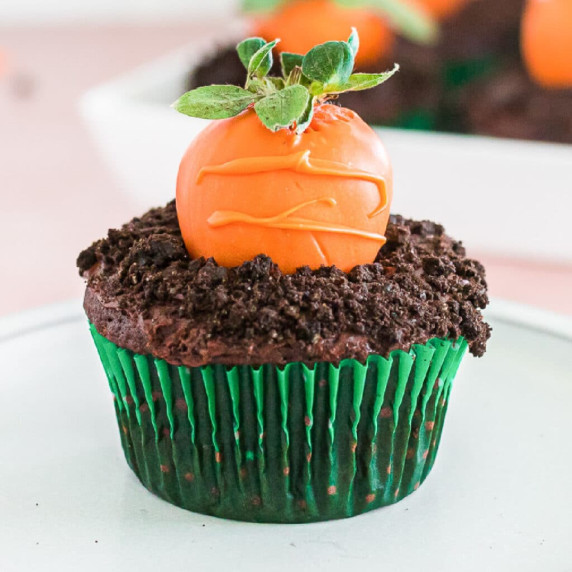 Close up of a cupcake with an orange chocolate covered strawberry decorated to look like a carrot.