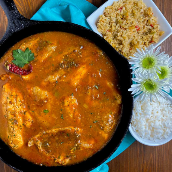 A white bowl filled with Cajun Catfish Courtbouillon with white flowers and a teal napkin. 