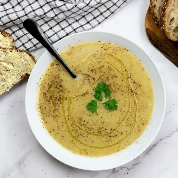 top down shot of soup in white bowl flanked with a tea towel and crusty bread