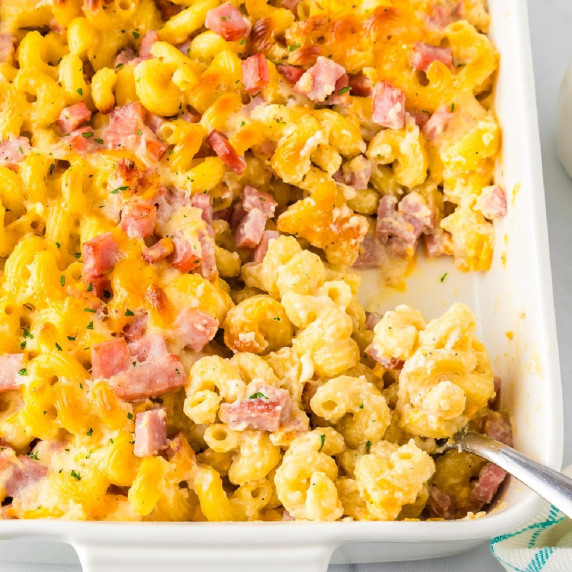 A serving pan filled with baked cavatappi macaroni & cheese topped with diced ham and melted cheese.