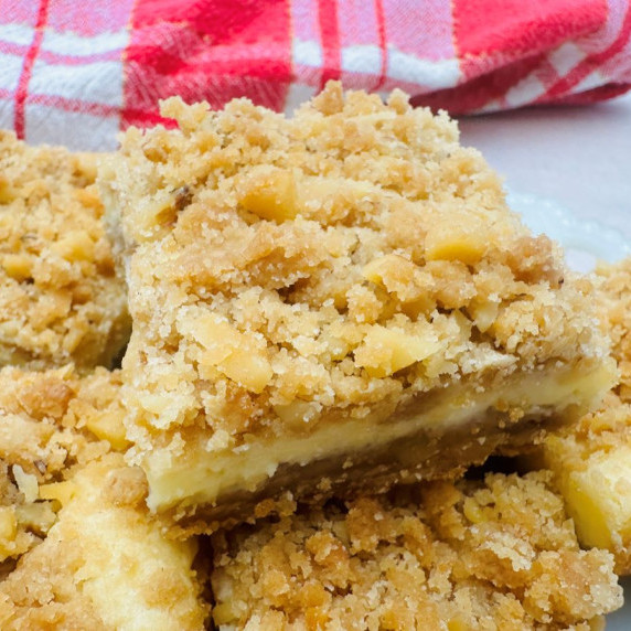 Close up of cheesecake bar with light brown crust, white filling, and crumb topping.
