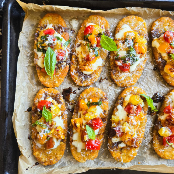 A tray of golden hashbrowns topped with colourful bruschetta and pops of green basil.