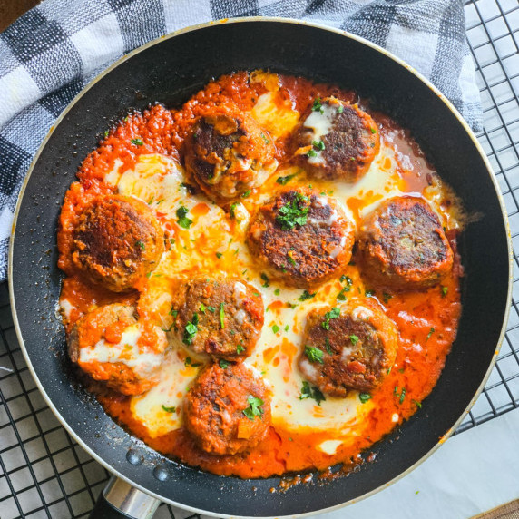 Cheesy skillet of meatballs with orange sauce against a checkered towel.