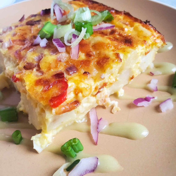 Potato casserole with a golden crust, purple onions, and greens.
