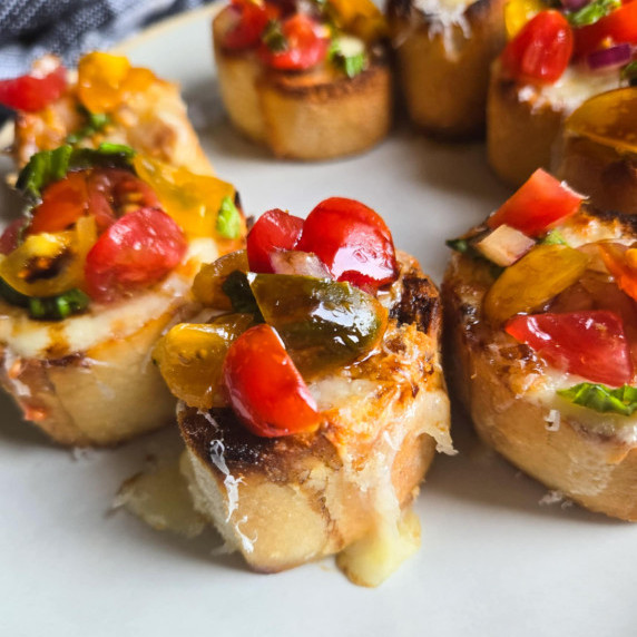Golden crostini topped with colourful bruschetta on a white plate.