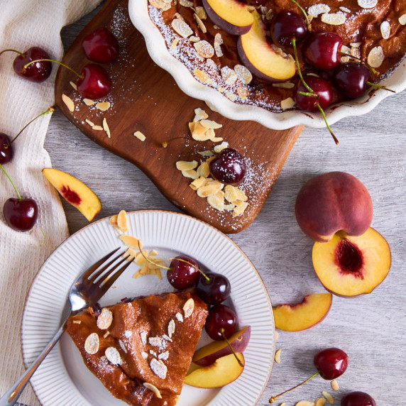 Cherry Peach Clafoutis with Protein, whole baked in the oven, one slice on a plate with icing sugar