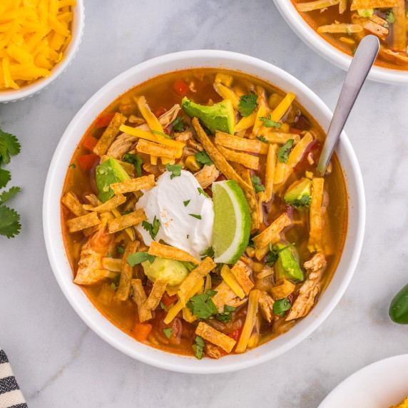 Bowl of chicken tortilla soup topped with tortilla strips, sour cream and a slice of lime.