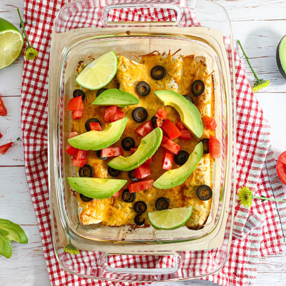 chicken enchiladas with olives, tomato, and avocado on a red check cloth on a whitewashed table