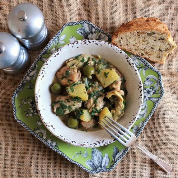 A bowl of chicken piccata stew on a green plate with bread and a fork