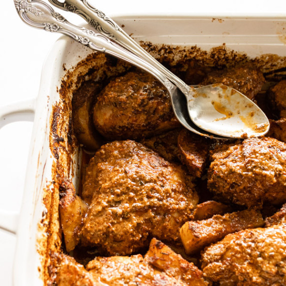 mediterranean baked chicken and potatoes in a white baking dish with serving spoons.