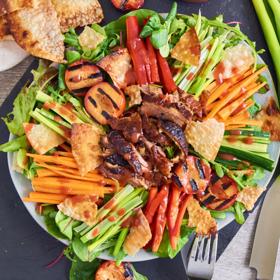 A plate of crispy duck pancake salad with baby leaves, different julienned veggies and plums