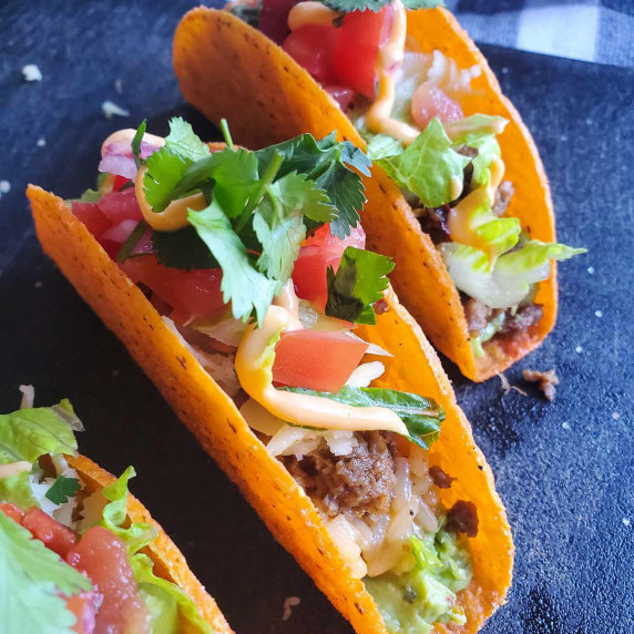 Cheesy taco shells stuffed with colourful toppings against a black background.